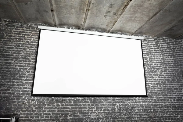 Angle view of white projector screen on gray brick wall — Stock Photo, Image
