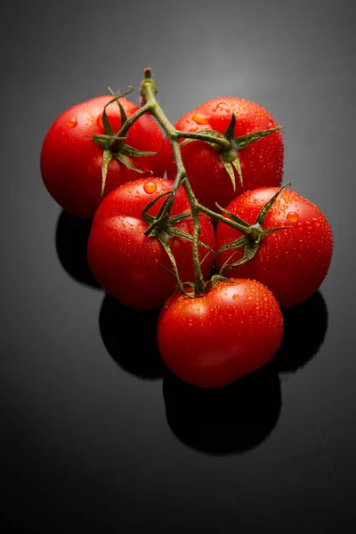 Imagem do molho de tomates frescos no fundo preto com reflexão e gotas de água — Fotografia de Stock