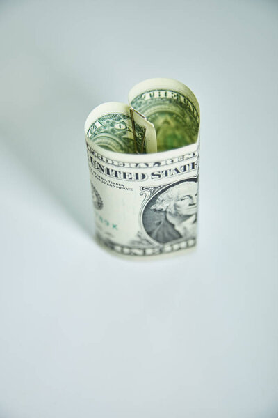 Heart folded from one dollar bill over gray background with copy space. Concept image of money love