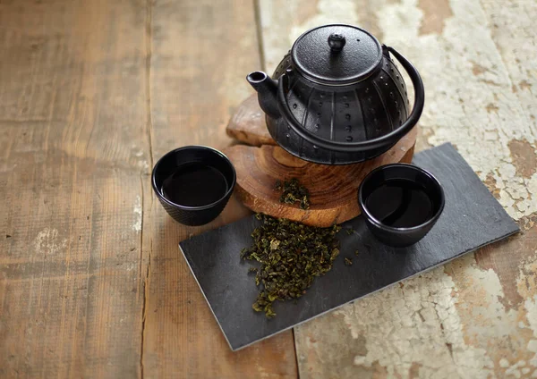 Green asian tea on vintage wooden table. Top side view of teapot and cups on black rock with copy space