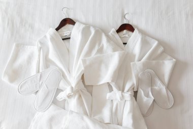 Otel odasındaki yatakta iki beyaz bornoz ve terlik.