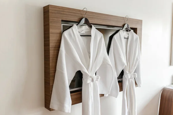 İki beyaz bornoz şık bir otel odasının içindeki ahşap askılarda asılı. Otelde iki dakika dinlen.
