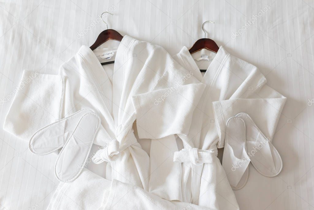 two white bathrobes and slippers on the bed in hotel room