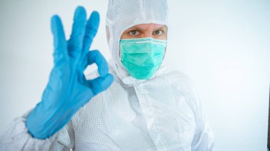 Beyaz erkek doktor koruyucu giysi ve maske takıyor evet işareti yapıyor, tamam işareti veriyor. Beyaz arka planda izole edilmiş. Tıbbi ve sağlık hizmetleri konsepti. Biyolojik tehlike