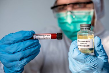 Koruyucu giysili bir erkek bilim adamı koronavirüs aşısı taşır. Negatif test tüpü ve enfekte kan örneği taşıyan beyaz bir adam ve COVID-19 aşısı. 2019-NCoV Wuhan Çin 'de bulundu..