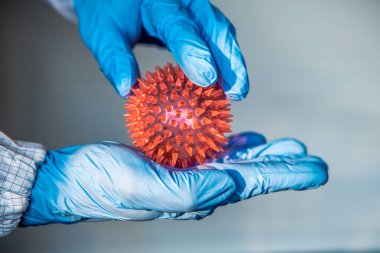 Coronavirus kırmızı bir model taşıyan koruyucu giysili bir bilim adamı. COVID-19 molekülü. İnsanlar arasında virüs bulaşması ya da bulaşması. Tıbbi ve sağlık hizmetleri, biyolojik tehlike.