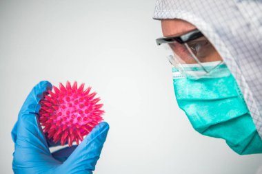 Corona virüsü modeli olan bir tıp doktoru. Korunma giysisi giymiş, elinde Coronavirus tutan bir erkek bilim adamı. Coperid-19 molekülü olan beyaz bir adam. MERS-Cov virüsünün soyut bir modeli.