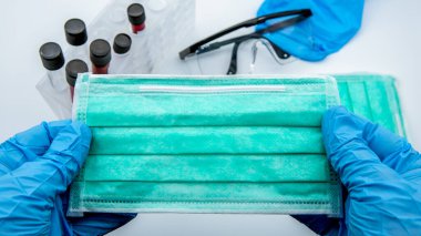 Mavi eldiven giyen ve beyaz arka planda yeşil bir tıbbi maske takan bilim adamları. Tek kullanımlık maskeler ağız ve burnu kapatır. Bakterilere karşı konsept koruma, Coronavirus COVID-19