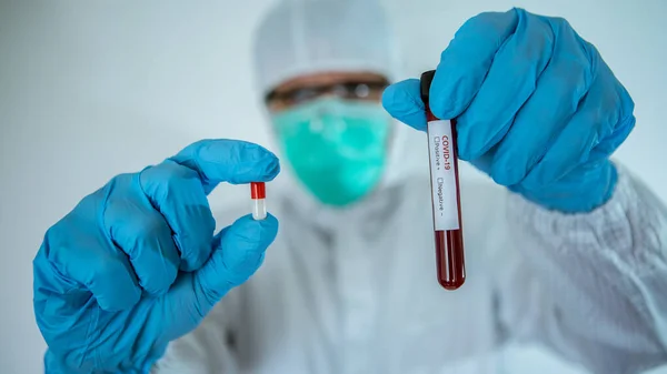 Doctor in laboratory holding a pill and blood test tube on white background. Covid-19 is currently trying to find a drug against the virus to treat the infected. Vaccine to cure coronavirus concept.