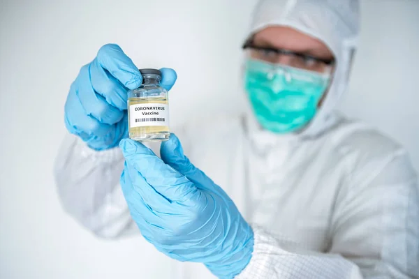 A caucasian doctor in laboratory holding a liquid vaccines for coronavirus diseases. Male scientific on protective suit with a vaccine Covid-19. Medical and health care concept, Biological hazard.