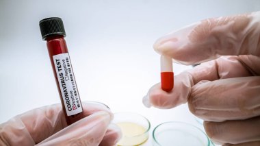Roman Coronavirus hapı ve beyaz arka planda kan testi tüpü. Covid-19 şu anda virüse karşı virüsü tedavi edecek bir ilaç bulmaya çalışıyor. 2019-NCoV konseptini tedavi edecek haplar.