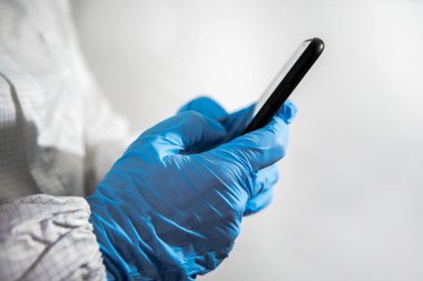 Bilimsel kimya laboratuvarında akıllı telefon kullanan bir bilim adamı. Doktor elleri mavi eldivenli, telefon cihazı kullanıyor. Coronavirus acil duruma neden oldu. Covid-19 pandemik karantina kavramı