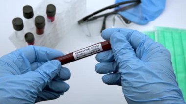 4K, yüz maskesi ve COVID-19 için enfekte kan örneği içeren test tüpü, Wuhan, Çin 'de bulunan yeni bir coronavirüs. Koruma için mavi eldivenli bilim adamı. 2019-nCoV-Dan virüsü için aşı araştırması