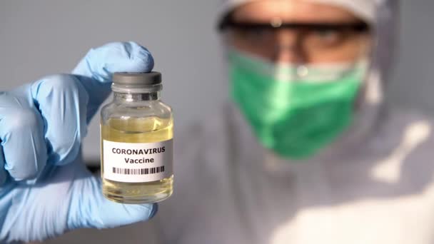 研究室の白人医師はコロナウイルス症のための液体ワクチンを持っています ワクチンCovid19で保護服の男性科学者 医学と医療の概念 生物学的危険ダン — ストック動画