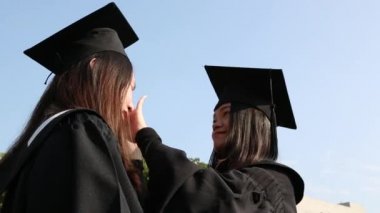 Mezuniyet gününde heyecanlı Asyalı arkadaş grubunun portresi. Arka planda üniversite binası olan doğal yeşil bir arazide kampüsün dışındalar.