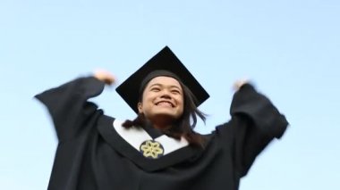 Mezuniyet gününde heyecanlı Asyalı arkadaş grubunun portresi. Arka planda üniversite binası olan doğal yeşil bir arazide kampüsün dışındalar.