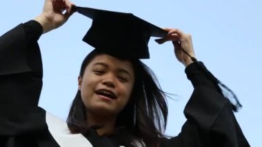 Mezuniyet gününde heyecanlı Asyalı arkadaş grubunun portresi. Arka planda üniversite binası olan doğal yeşil bir arazide kampüsün dışındalar.