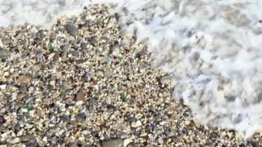 Tayvan Adası 'nda dalgaların köpüğüyle okyanus kıyısında yavaş hareket eden peebles plajı. Deniz sörfleri çok renkli renkli taşların üzerine sıçrıyor. Kıyıdaki dalga, Dan.