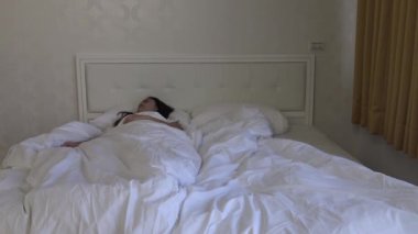 4k, yatakta uyuyan güzel Asyalı kadın uyanıyor ve pencereye bakıyor.