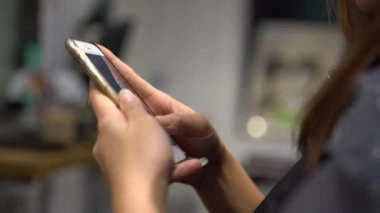 Kuaförde akıllı telefon kullanan 4K Asyalı kadın sohbet etmek ve insanlarla iletişim kurmak için ekrana dokunuyor. İnternette sörf yapmak için iyi bir zaman, sosyal ağları kontrol etmek ve onun telefon cihazına yapılan metinleri yazmak için.