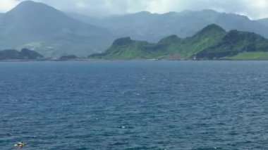 4K, tropik Tayvan adasında yeşil dağ ve bulutlarla mavi okyanus suyunda dalış yapan bir grup. Yaz tatilinde insanlar denizde yüzüyor. Güzellik manzarası Dan.