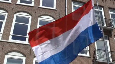 Amsterdam 'da bayrak direğinde rüzgarda dalgalanan Hollanda bayrağı. Geleneksel ev arka planda. Gerçek bir kumaş dokusunu kapat Asteğmen çırpınan Dan