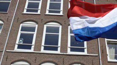 Amsterdam 'da bayrak direğinde rüzgarda dalgalanan Hollanda bayrağının yavaş hareketi ve geleneksel bir ev. Gerçek bir kumaş dokusunu kapat Asteğmen çırpınan Dan