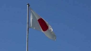Japonya bayrağı bayrak direğinde rüzgarda sallanıyor. Mavi gökyüzü rüzgarlı bir günde Japon bayrağı dalgalanır. Gerçek bir kumaş dokusuna yaklaş. - Dan.