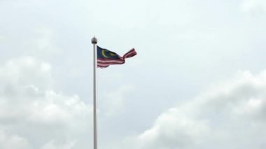 Kuala Lumpur şehrinde bulutlu bir havada bayrak direğinde dalgalanan Malezya bayrağının yavaş hareketi. Malezya bayrağı karanlık gökyüzünde dalgalanıyor. Gerçek bir kumaş dokusunu kapat Asteğmen çırpınan Dan