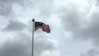 Kuala Lumpur şehrinde bulutlu bir havada bayrak direğinde dalgalanan Malezya bayrağının yavaş hareketi. Malezya bayrağı karanlık gökyüzünde dalgalanıyor. Gerçek bir kumaş dokusunu kapat Asteğmen çırpınan Dan