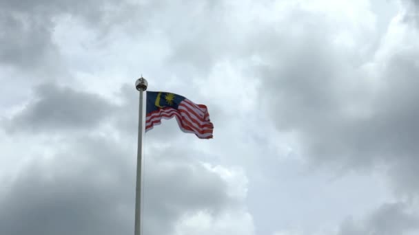 在多云天气下 马来西亚国旗在吉隆坡的旗杆上缓缓飘扬 马来西亚的旗帜在漆黑的天空中飘扬 一个真正的面料纹理的特写标志着飘扬 — 图库视频影像
