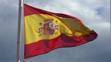 Bir şehirde bayrak direğinde rüzgarda sallanan İspanyol bayrağının yavaş hareketi. İspanya bayrağının yavaş çekimde dalgalanması mavi gökyüzünün önünde. Gerçek bir kumaş dokusunu kapat Asteğmen çırpınan Dan