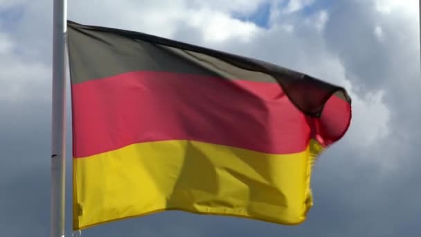 市内の旗竿にドイツ国旗が風に揺れるのが遅い 青空の前でドイツのバナーフラッターのスローモーション 生地の質感を閉じますエンサインなびかせダン — ストック動画