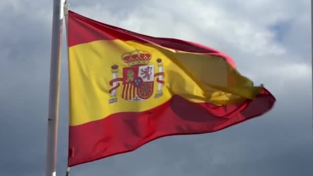 在城市的旗杆上 西班牙国旗缓缓地在风中飘扬 西班牙国旗在蓝天前缓缓飘扬 一个真正的面料纹理的特写标志着飘扬 — 图库视频影像