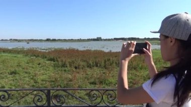 4K, Asyalı Kadın Ulusal Park-Dan 'da Atlar bataklıkta otlarken A Grubu Pembe Flamingo' nun akıllı telefonuyla bakıyor ve fotoğraf çekiyor.