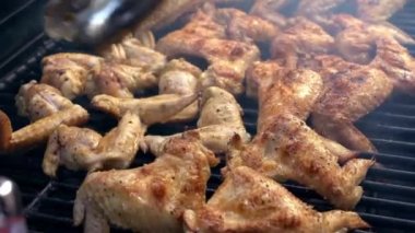 Barbeküde ızgara yapılan baharatlı tavuk kanatlarını döndürmek için metal maşa kullanan bir adam. Barbekü ızgarasında dönen çok lezzetli kızarmış tavuk eti kanatları. Şef arka bahçede yemek pişiriyor. Dan.