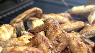 Yavaş Çeken Adam, ızgarada ızgara yapılan baharatlı tavuk kanatlarını döndürmek için metal maşa kullanıyor. Barbekü ızgarasında kızarmış tavuk eti kanadı var. Şef arka bahçede yemek pişiriyor. Dan.