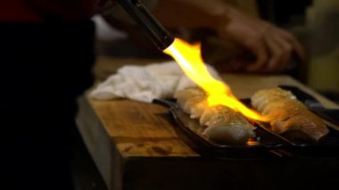 Asyalı şef sushi karamelize yapmak için pürmüz ile bir dilim çiğ balık yakar. Japon restoranında yemek yapan bir adam. Japonya 'da mutfak arka planında taze sashimi pişirip yakmak. - Dan.