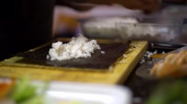 4K, suşi ve rulo yapmak için beyaz pilav. Erkek aşçının elleri evde ya da mutfak masasındaki restoranda geleneksel Japon yemeklerini hazırlıyor. Hazırlık aşamasında Makizushi - Dan