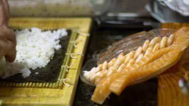 Suşi ve rulo yapmak için yavaş pilav hareketi. Erkek aşçının elleri evde ya da mutfak masasındaki restoranda geleneksel Japon yemeklerini hazırlıyor. Hazırlık aşamasında Makizushi - Dan