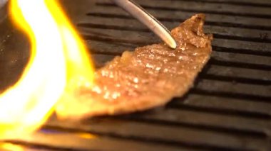 Ağır çekimde, sıcak kömürde dilimlenmiş et ızgarası. Restoran barbeküsünde Japon yemeği. Japon BBQ Yakiniku usulü ızgara et.