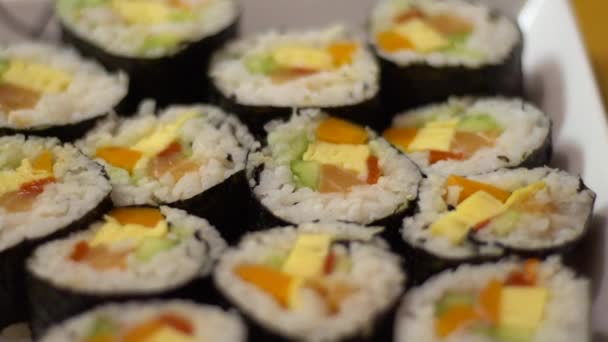 スローモーションホワイトプレートで提供されるサーモンとおいしい巻き寿司セット レストランで伝統的な巻き寿司日本料理 ご飯の上に海苔と魚がのったグルメメニューです Dan — ストック動画