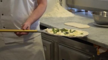 Kürek üzerinde taze İtalyan pizzasının yavaş çekimleri geleneksel ahşap yakılmış taş fırınına konuyor. Aşçı fırına pişmemiş pizza koyuyor. Kır mutfağında fast food pişiriyorum.