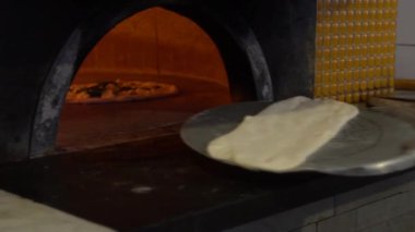 Kürek üzerinde taze İtalyan pizzasının yavaş çekimleri geleneksel ahşap yakılmış taş fırınına konuyor. Aşçı fırına pişmemiş pizza koyuyor. Kır mutfağında fast food pişiriyorum.
