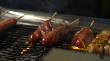 Slow Motion Sendor, Çelik Izgara Gece Pazarı caddesinde Tayvan sosisi pişiriyor. İnsanlar et ızgara barbekü yaptı. Kömürün alevi. Lezzetli ızgara yemekler. Çin sosisli sandviçi, Asyalı tezgah-Dan.