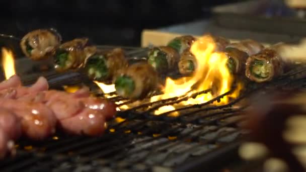 慢动作供应商在亚洲夜市街上的钢制烤架上煮咸肉葱包起来 人们烹调受欢迎的烤肉烧烤 燃烧的木炭 著名的市场 美味的食物 — 图库视频影像