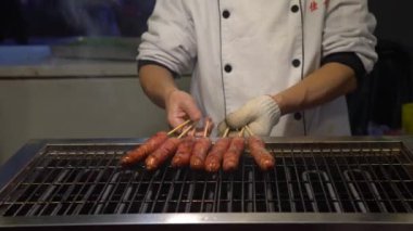 Asya 'daki Taipei Gece Pazarı' nda popüler barbekü sosisi pişiren 4K Asyalı insanlar.