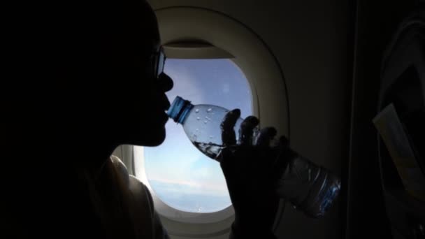 亚洲女人在飞行途中举着透明的瓶装水 年轻的旅行者坐在靠近窗户的飞机上 蓝蓝的天空 旅游人士 — 图库视频影像