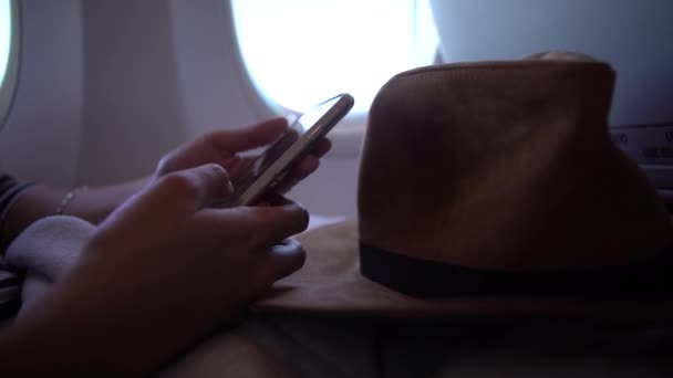 4K名亚洲妇女在飞行过程中手持智能手机 年轻的旅行者坐在飞机里面 用她的电话装置在飞机上留言 — 图库视频影像
