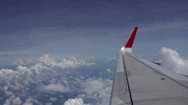 4K hava yoluyla seyahat ediyor. Uçak kanadı güzel gökyüzü ile uçuyor. Yukarıdan harika bulutlar, uçak penceresinden görüldüğü gibi. Kanatların ucu kırmızı. Kamaradaki gezginin görüntüsü - Dan